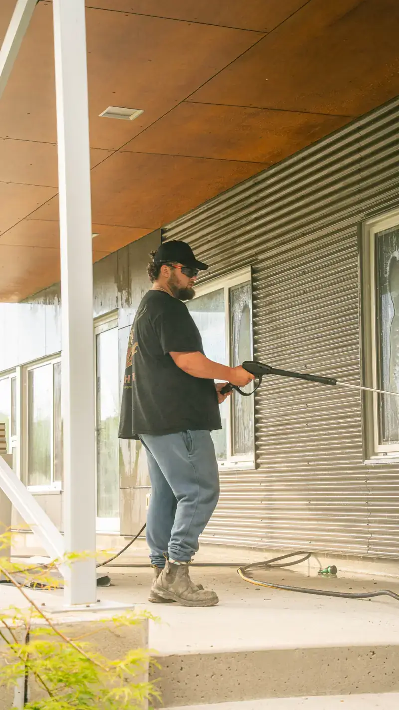 Technician pressure washing corrugated metal siding on a modern North Bay home