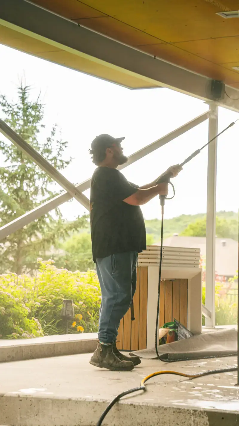 Crew member washing a covered porch ceiling with a pressure washer wand