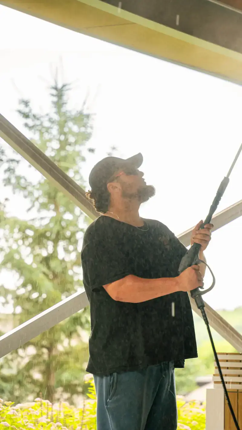 Close-up of a technician pressure washing overhead beams with mist in the air