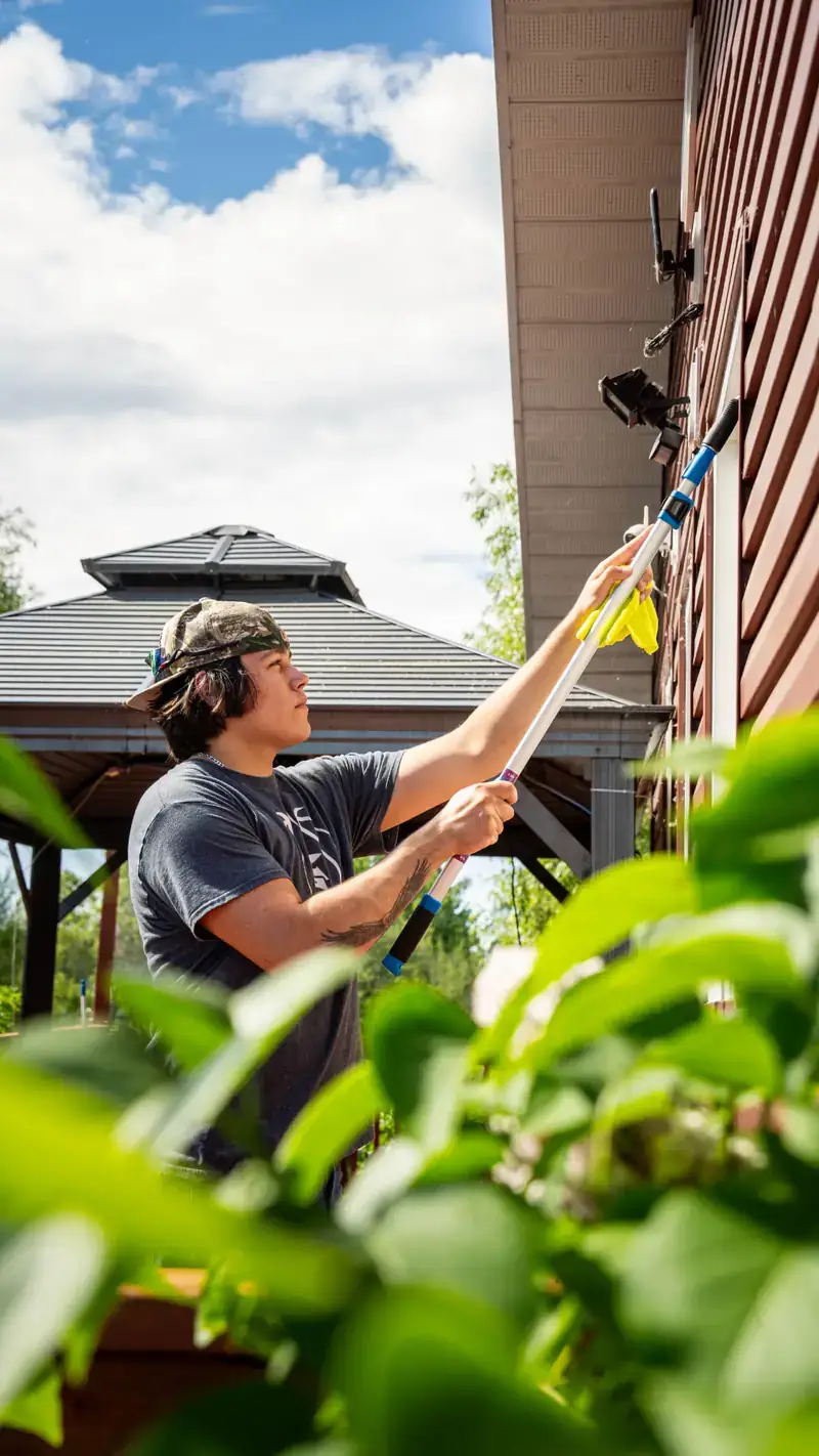 Nipissing Exteriors technician cleaning an upper-storey window with an extension pole in North Bay